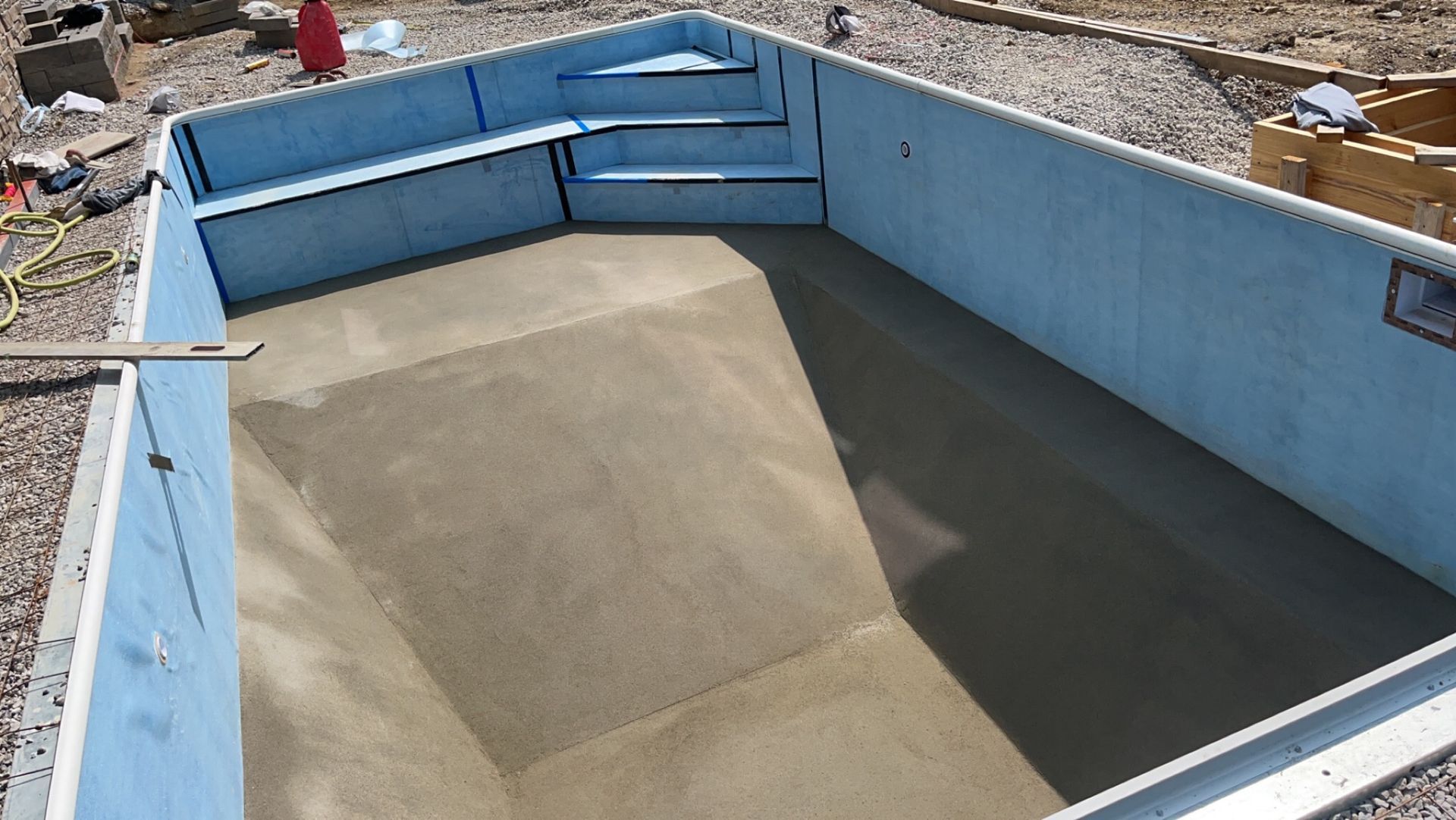 Pool under construction, light blue walls, gray concrete bottom, steps.