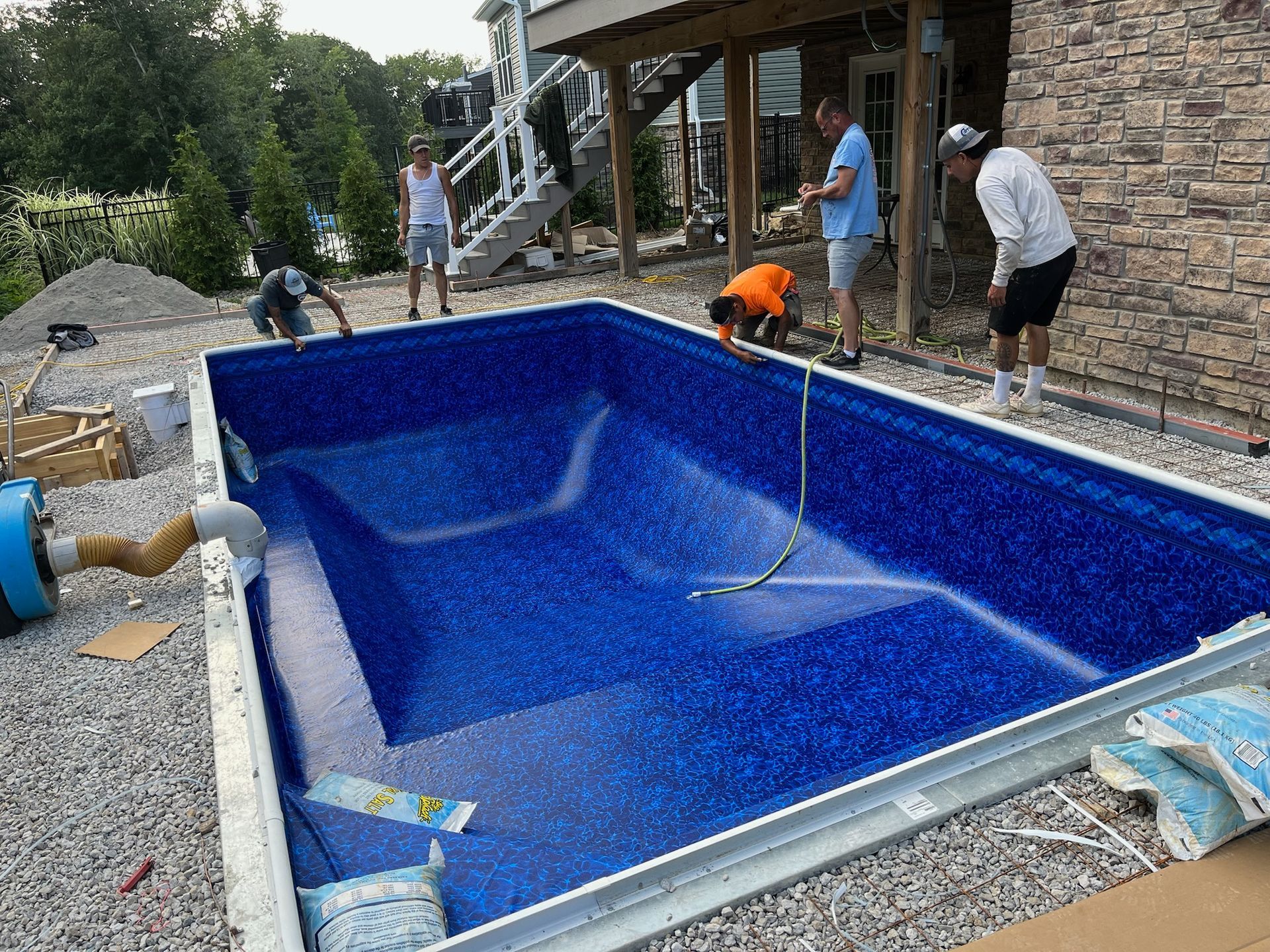 Pool construction: Workers installing a blue-tiled in-ground pool surrounded by gravel. People are working in the pool and surrounding it.