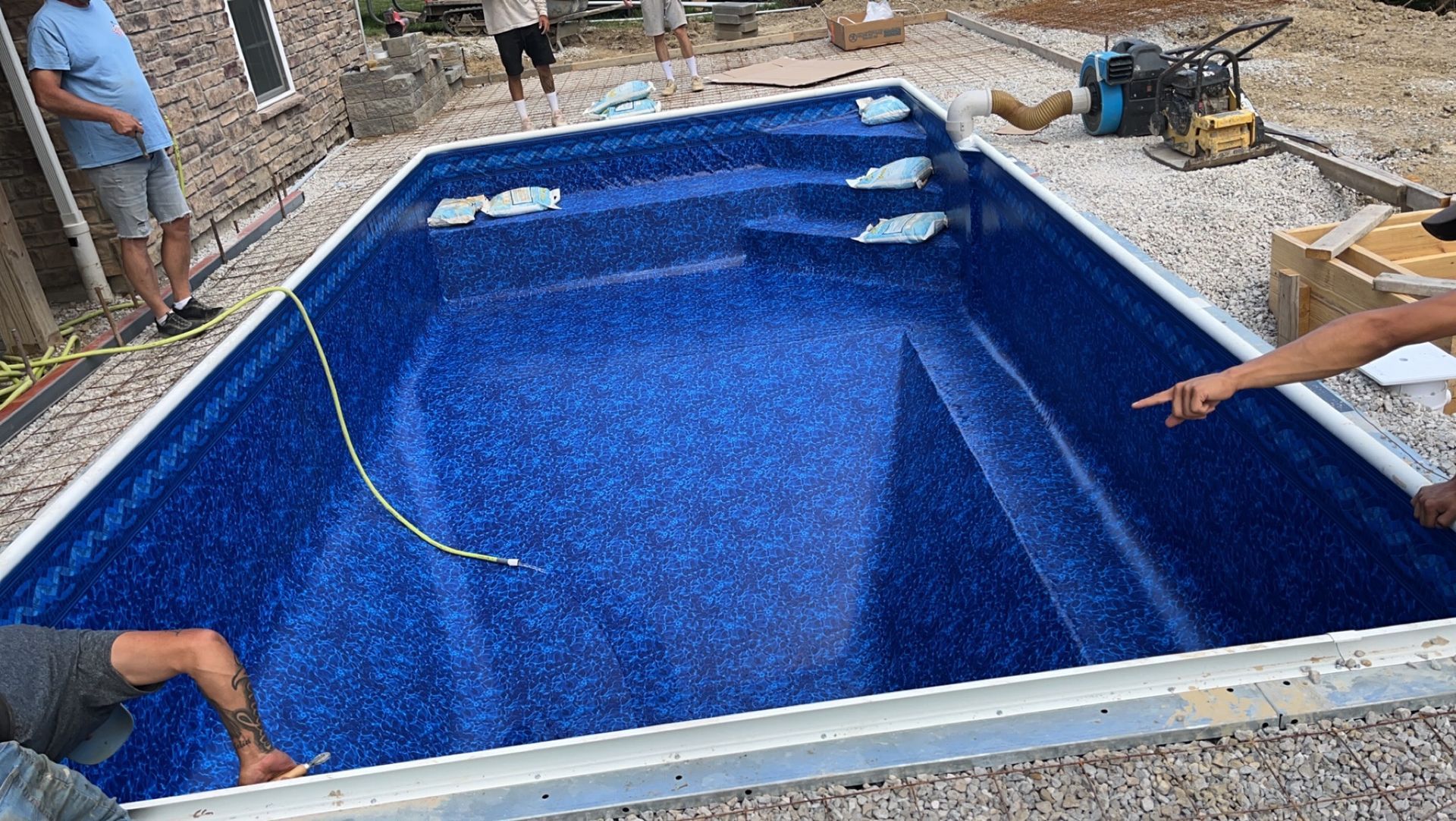Blue in-ground swimming pool under construction; workers installing liner.