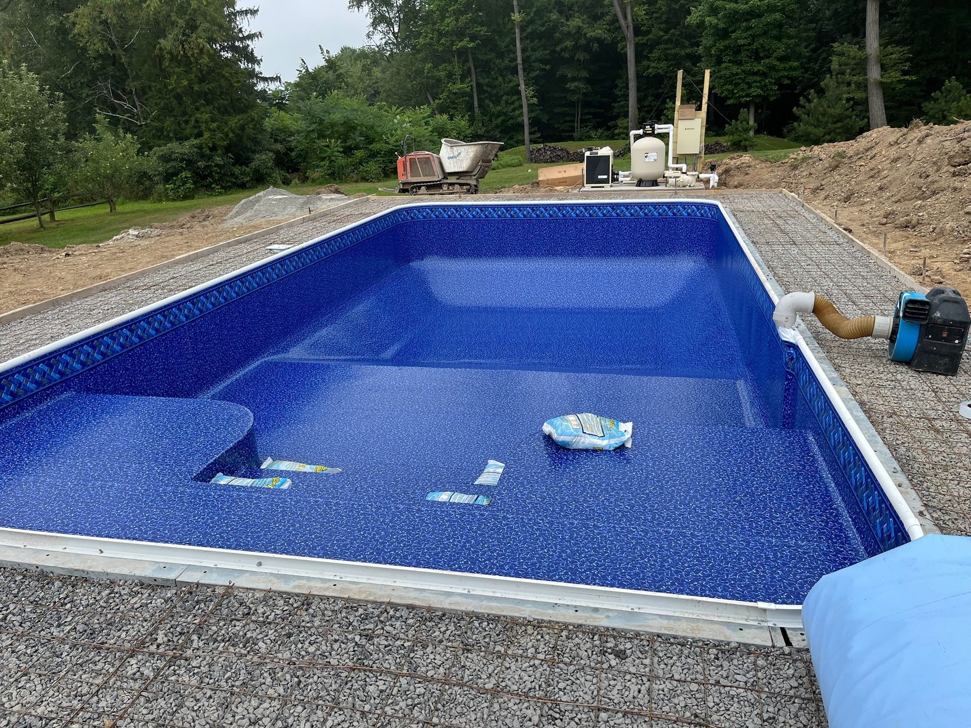Blue tiled pool under construction outdoors, surrounded by gravel and equipment.