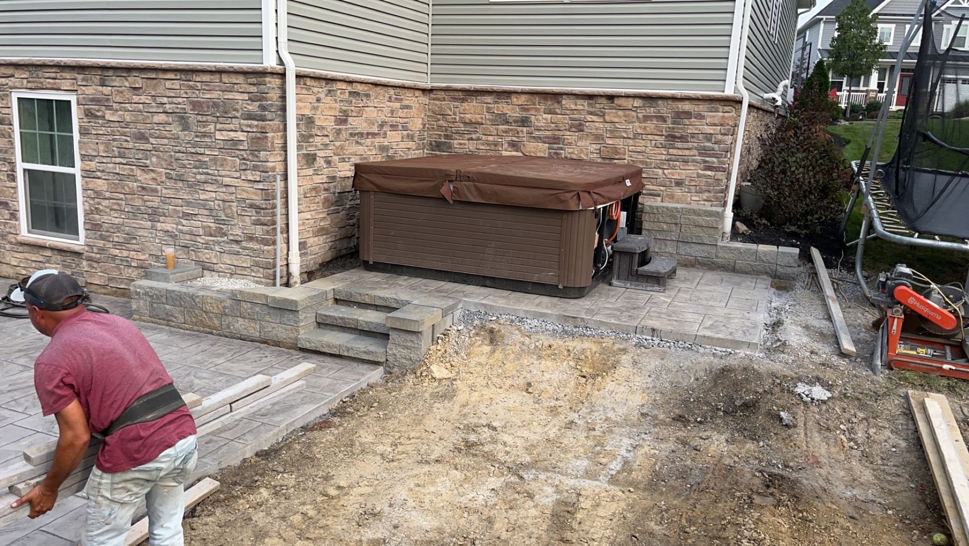 Man laying pavers near a hot tub installed beside a brick building.