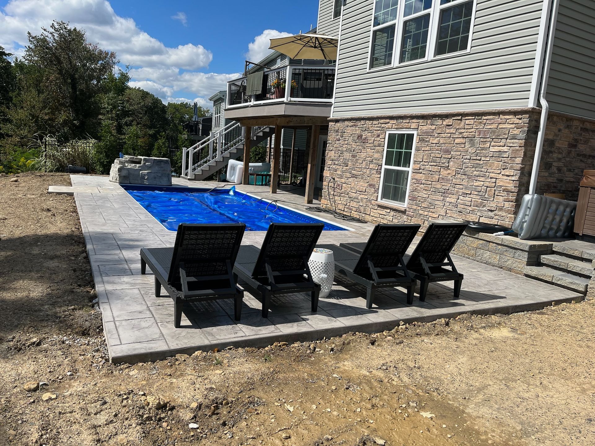 Lounge chairs by a pool covered with a blue tarp, beside a house with a deck.