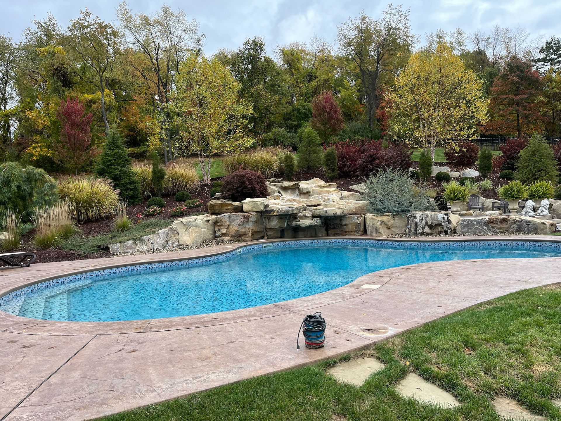 Pool with blue tile and rock waterfall, surrounded by colorful fall foliage.