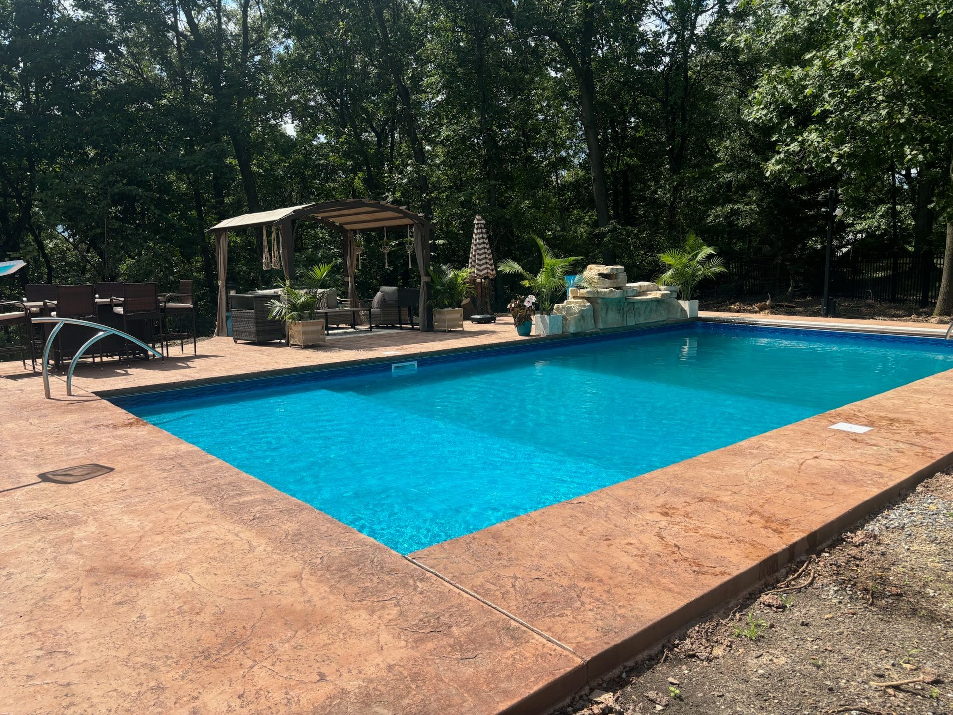 Swimming pool with stamped concrete border, trees, and pergola.