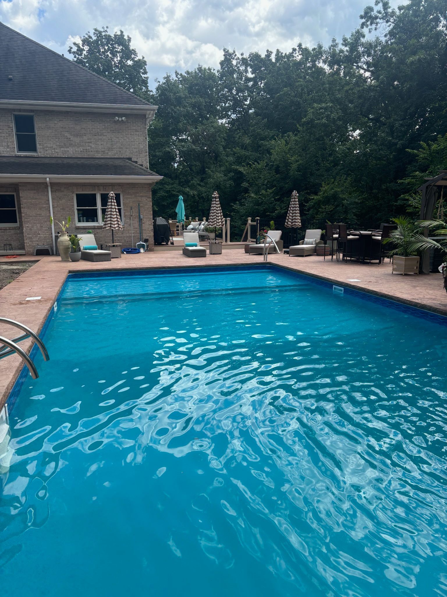 Swimming pool with blue water next to a house with trees and patio furniture.