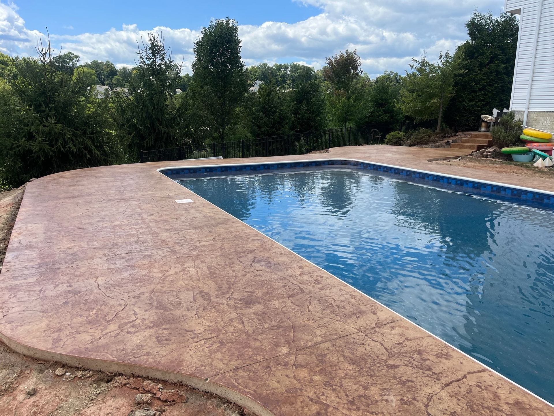 Pool with brown concrete edge, blue water, trees in the background, cloudy sky.