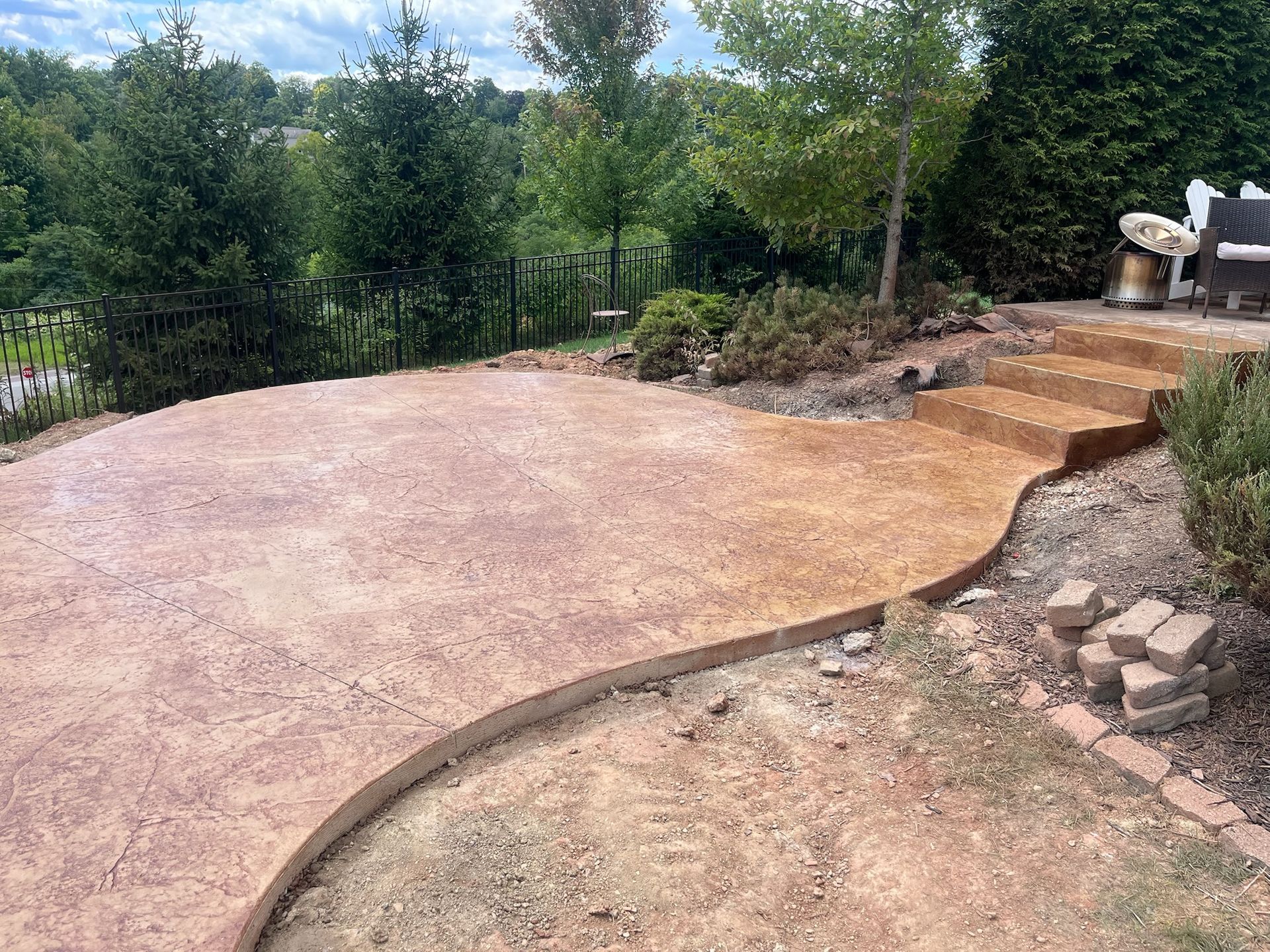 Curved concrete patio with steps leading up, surrounded by landscaping and trees.
