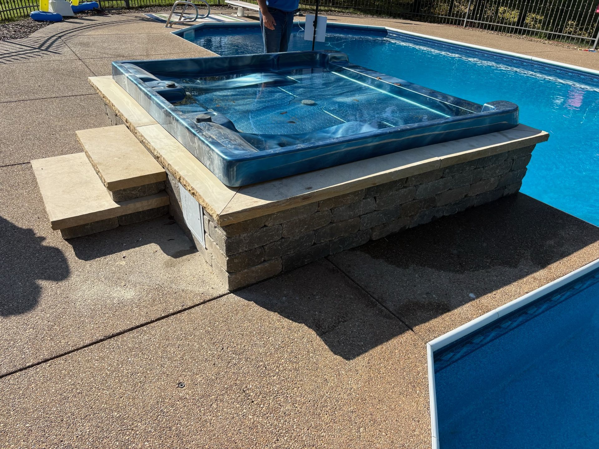 Hot tub on a raised platform next to a swimming pool. Steps lead up to the hot tub.