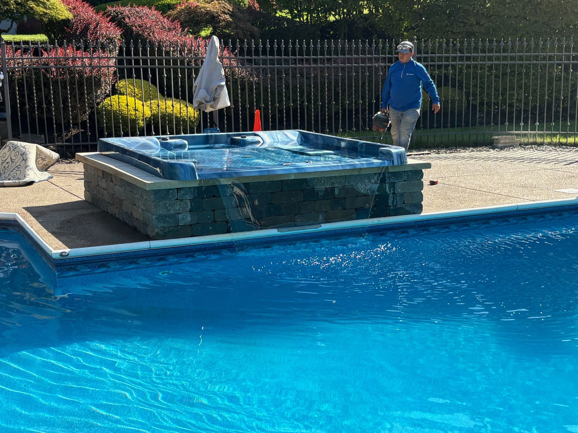 A person walks near a hot tub next to a pool. The hot tub is built into a stone structure.
