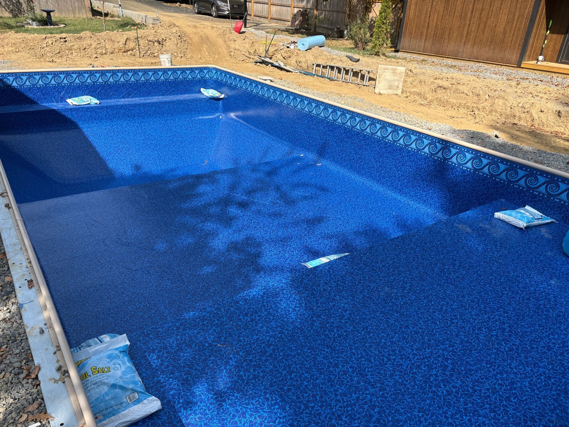 Blue-tiled swimming pool under construction, with cement borders and building materials surrounding.