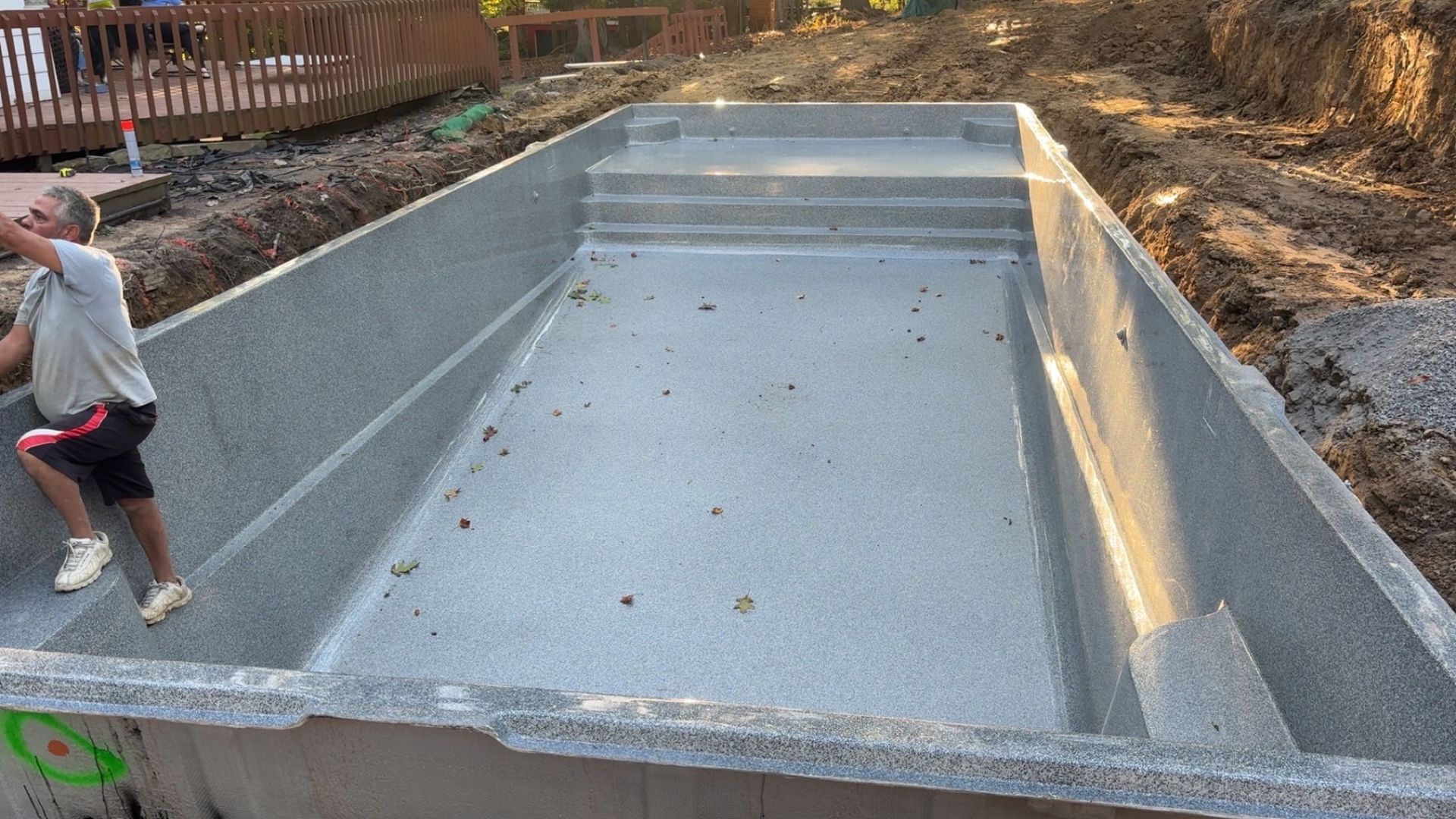 Man standing in unfinished pqool construction site; grey concrete pool with steps.