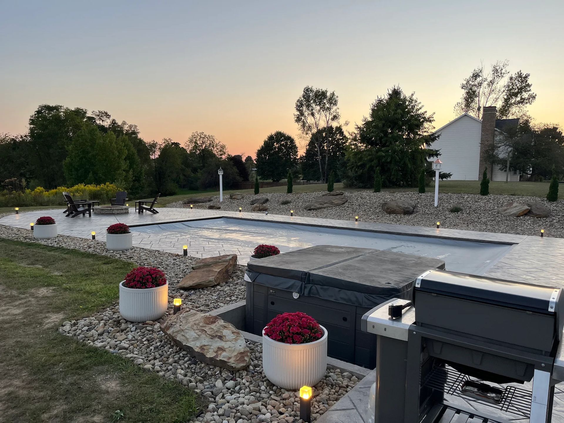 Outdoor area with pool, hot tub, grill, and landscaping at sunset.