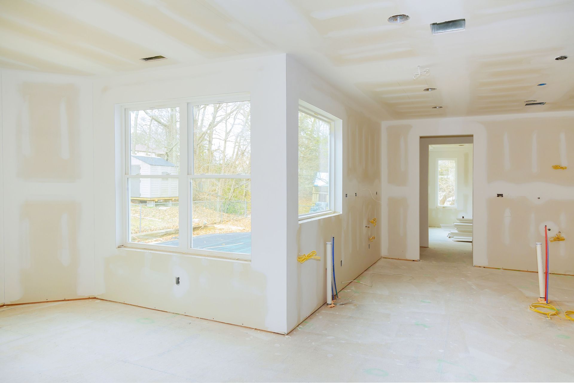 Bright unfinished room with large windows, white drywall, and bare floors in a new home.