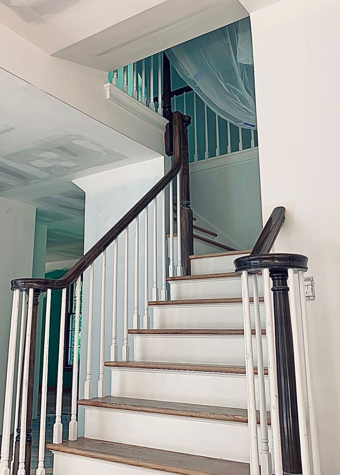 Indoor staircase with white steps, dark railing, and turquoise curtains in a bright home interior