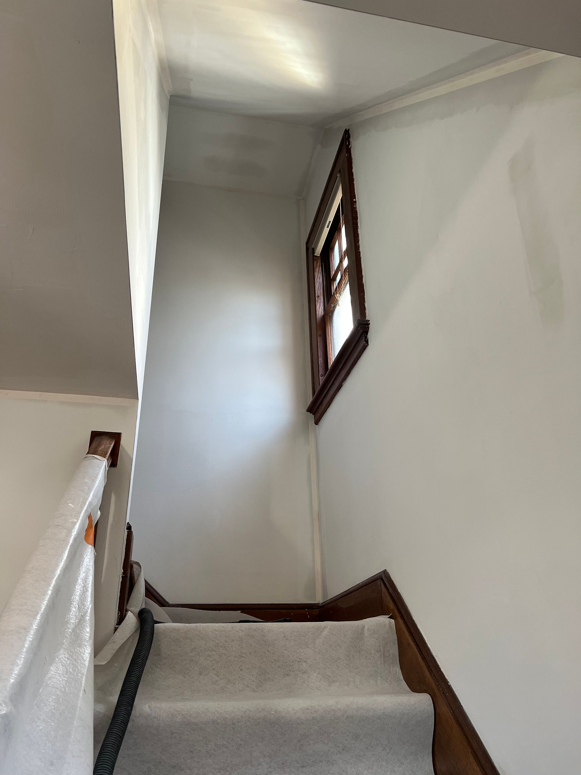 Narrow carpeted staircase with white walls and a window at the landing.