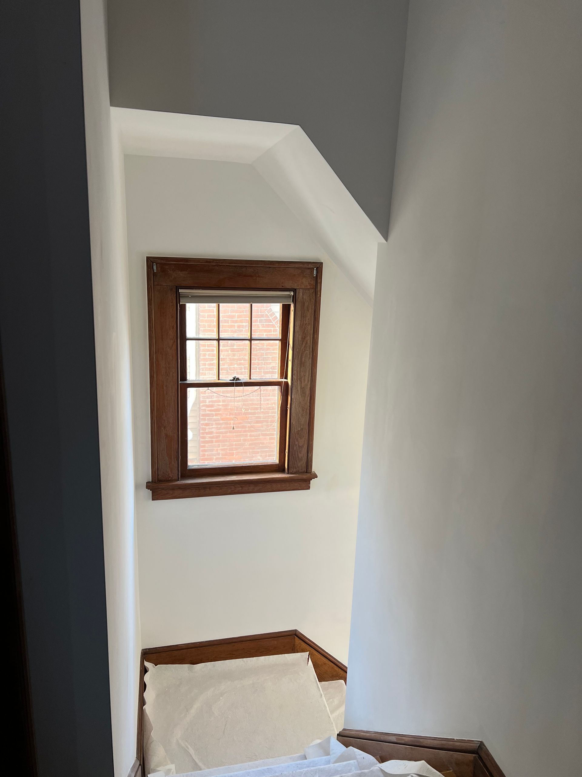 Narrow stair landing with a small wooden-framed window and white walls.