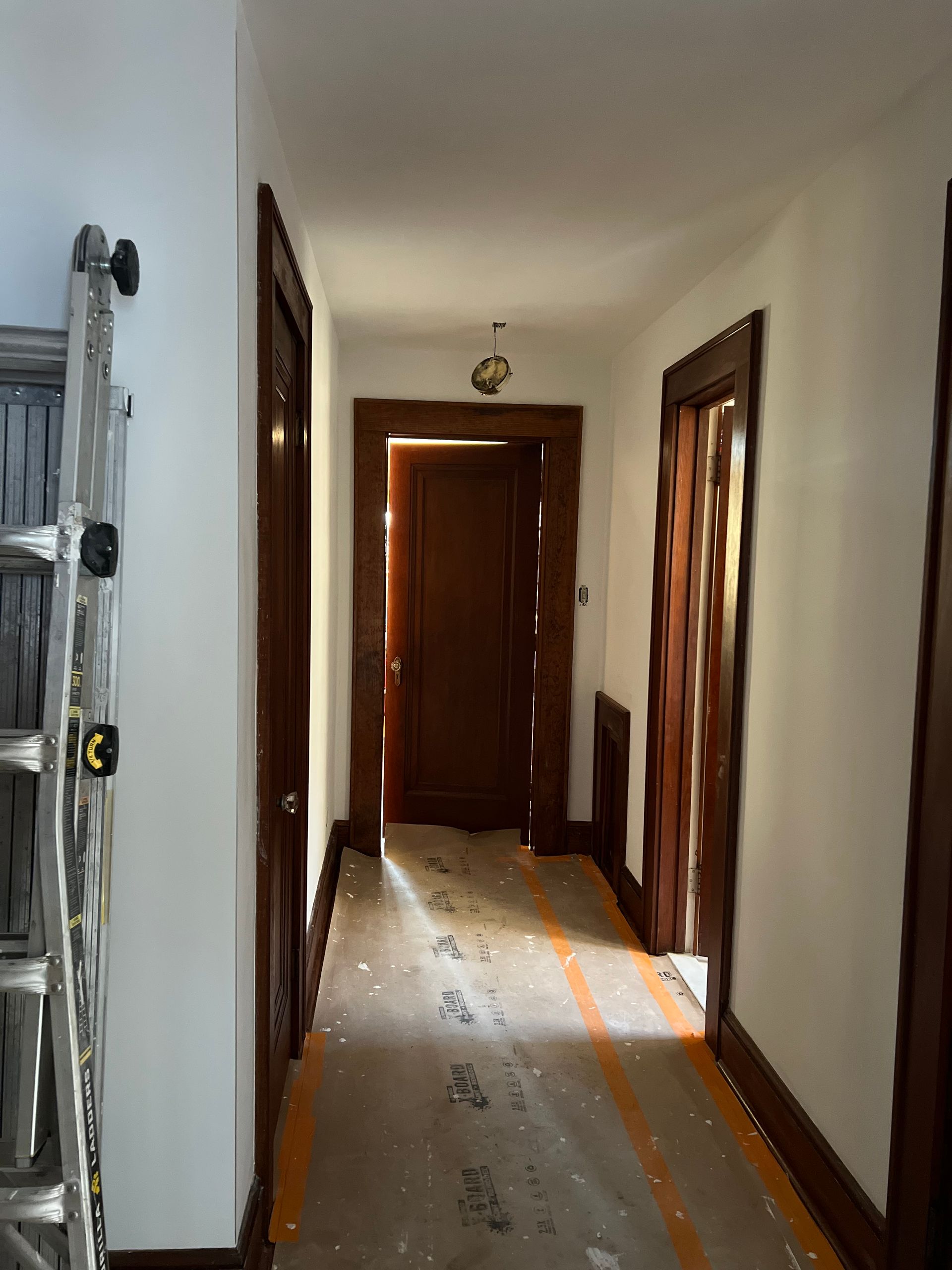 Narrow hallway with wooden doors, white walls, and a scuffed floor with orange tape lines.