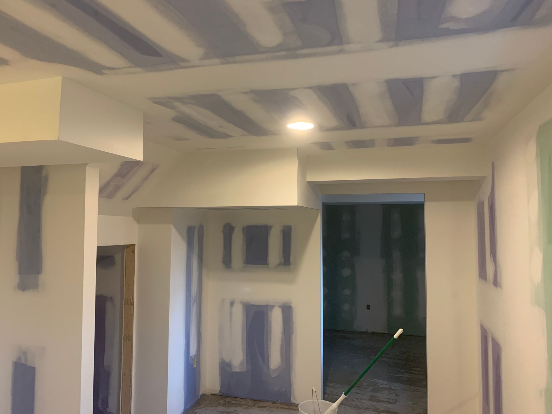 Renovation hallway with drywall patches, white walls, and an open doorway into a dark room
