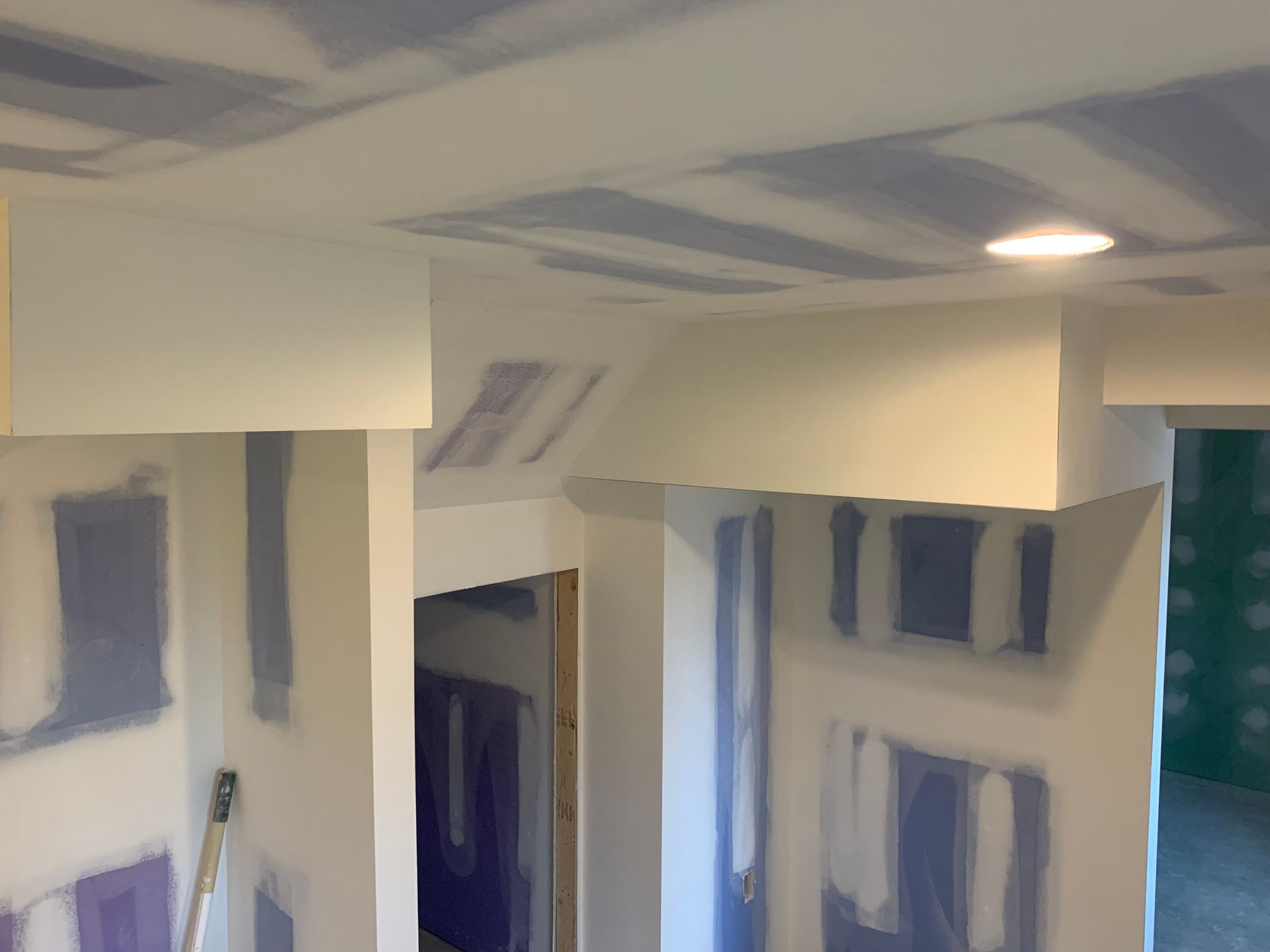 Partially painted room interior with white walls, blue-gray patching, and a doorway under construction