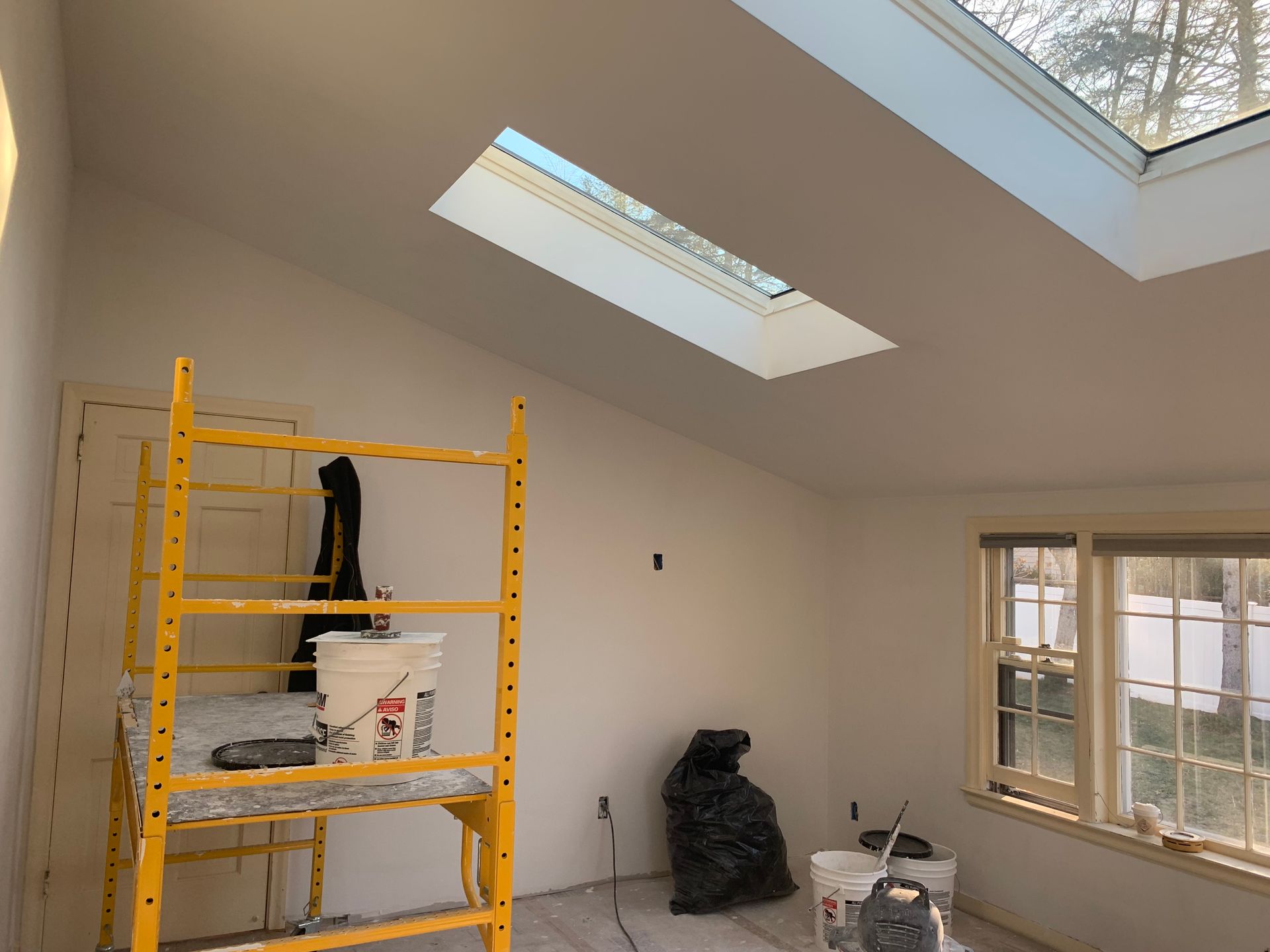 Renovated room with skylights, yellow scaffold, and windows under construction.