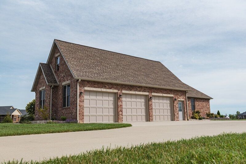 Brick three-car garage with beige doors and a brown roof, on a sunny day.