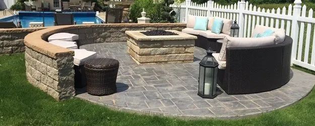 Stone outdoor patio with curved built-in seating, central fire pit, lantern, and wicker stools on pavers