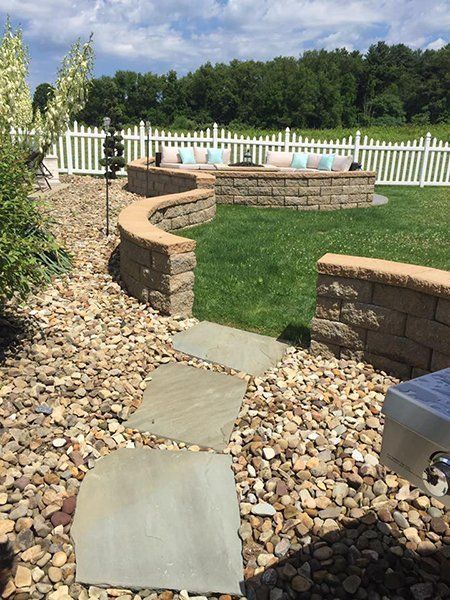 Backyard patio with stone path, curved retaining walls, and a fenced lawn near a pool