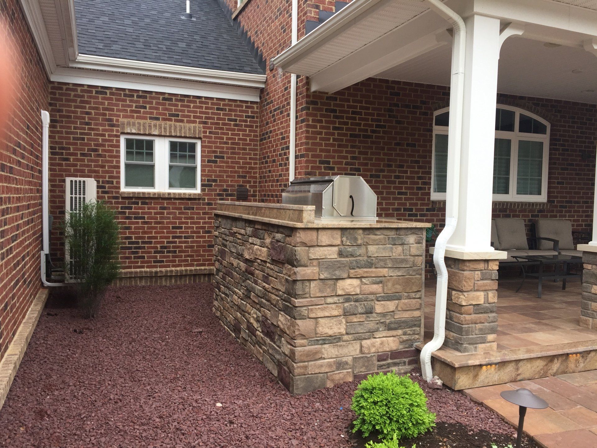 Brick house porch with stone steps, white columns, and a red gravel walkway in the front yard