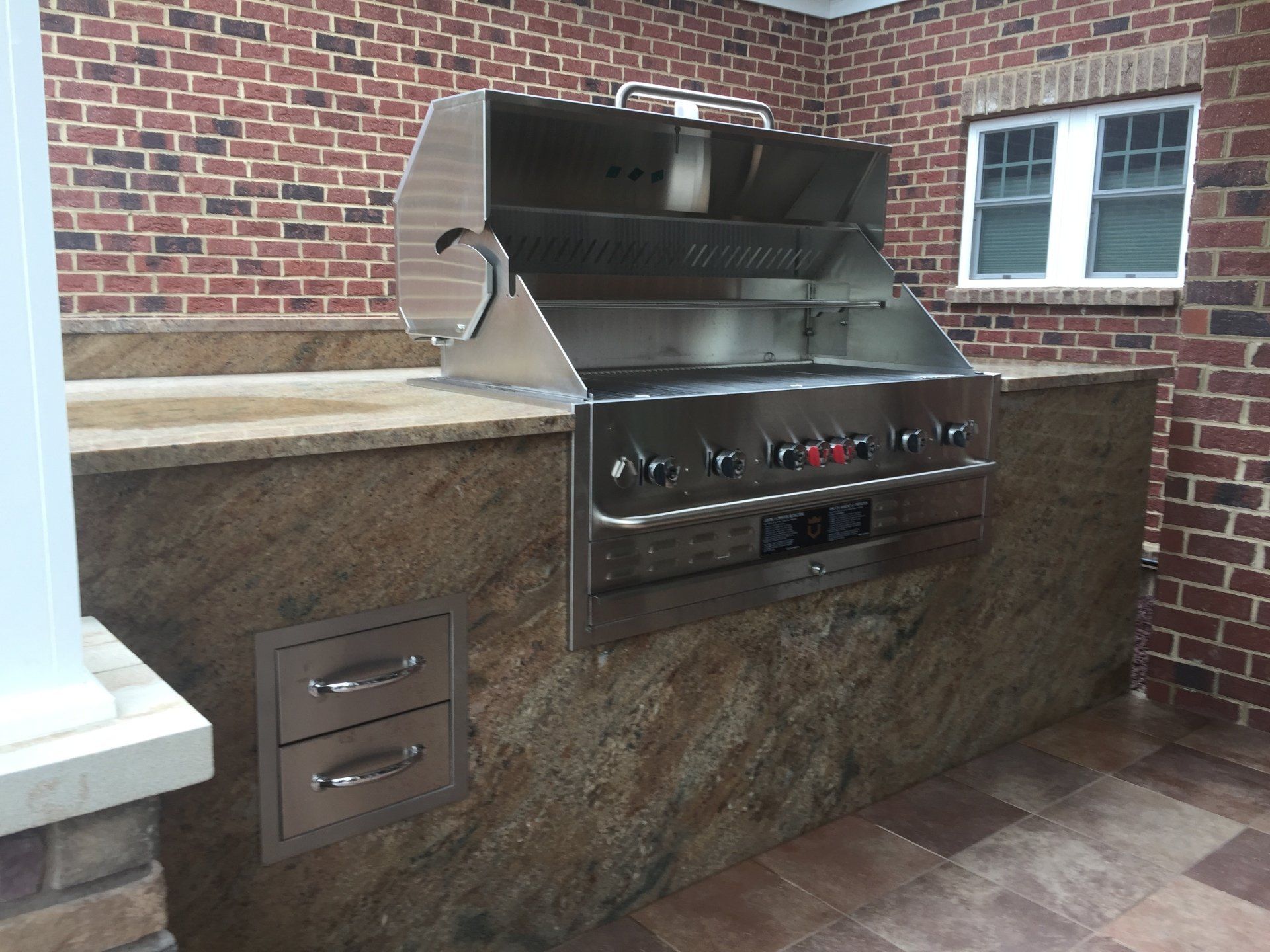 Outdoor built-in stainless steel grill with stone counter against a brick wall