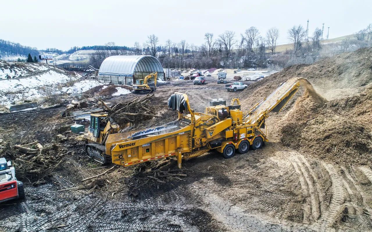 Yellow dump truck at a muddy construction site with debris and hills in the background