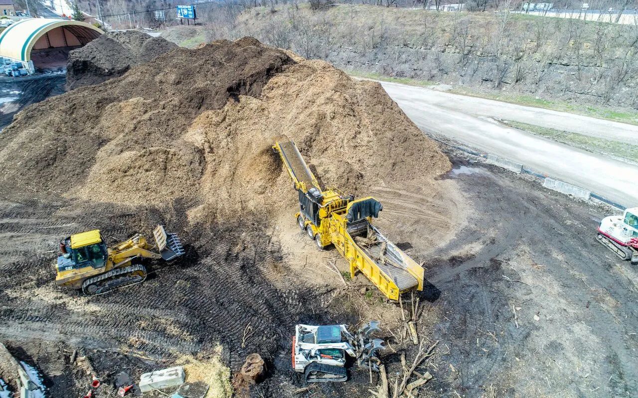 Construction site with excavators moving a large dirt pile beside a road tunnel entrance