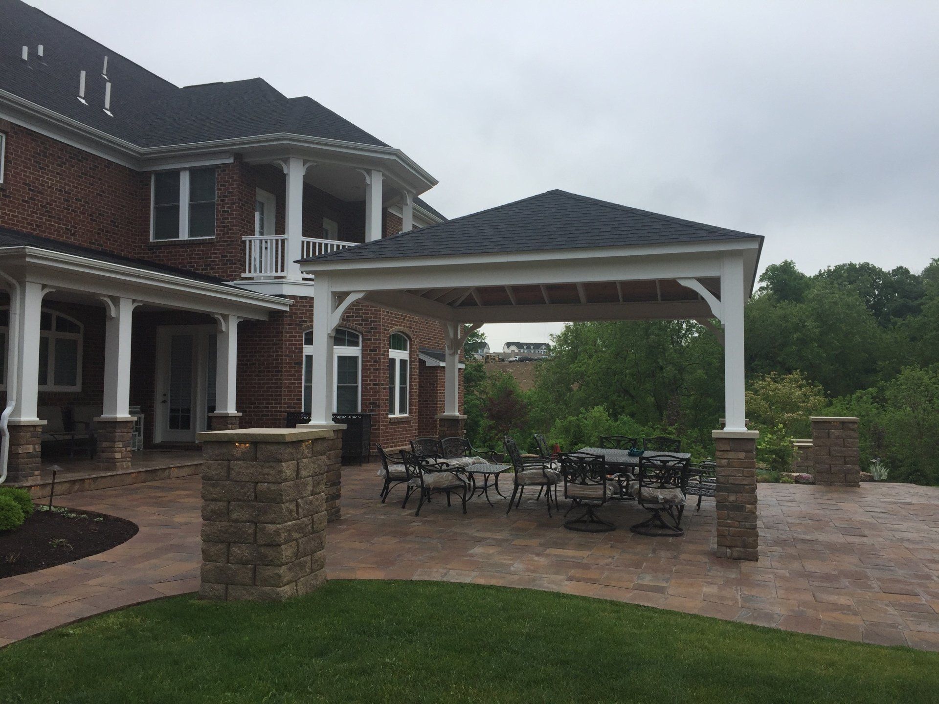Brick house patio with white columns, stone pavers, and outdoor dining under a covered pergola.