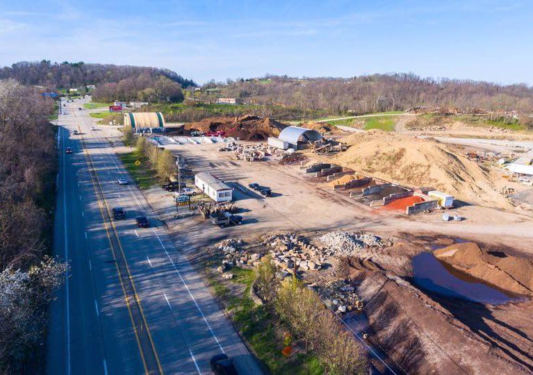 Aerial view of a road beside a large construction site with dirt piles, equipment, and a small pond.