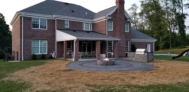 Large brick two-story house with a covered patio and circular stone fire pit in the backyard.