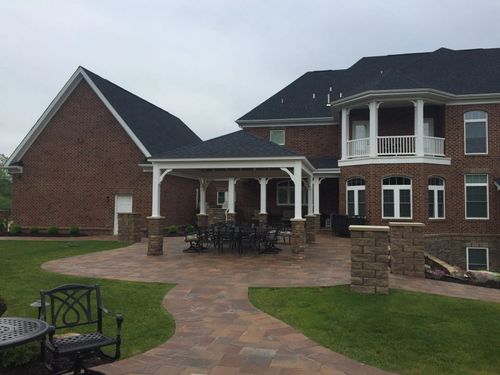 Brick house with a stone patio, covered outdoor seating area, and white columns in a landscaped yard
