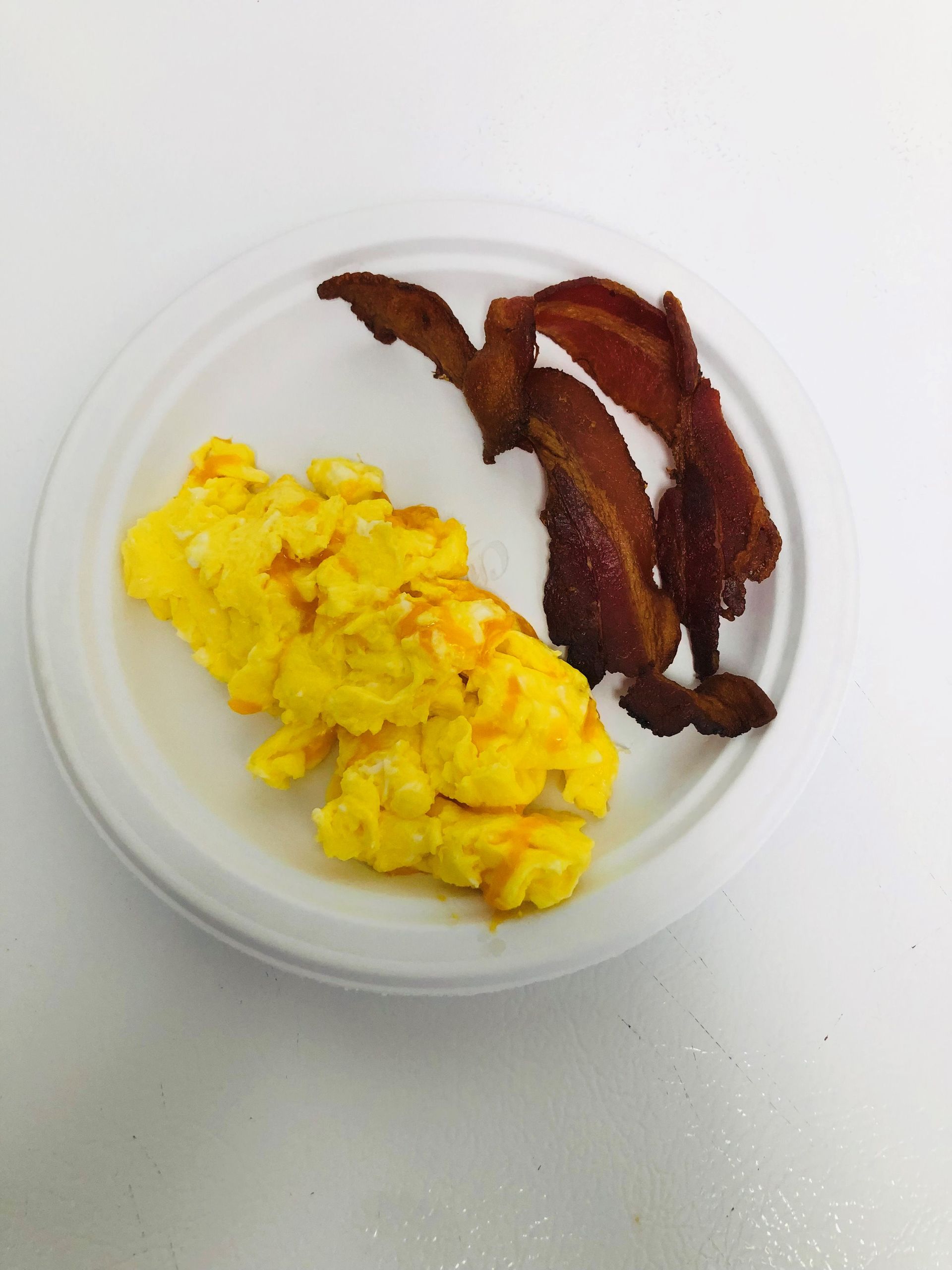 A white plate topped with scrambled eggs and bacon