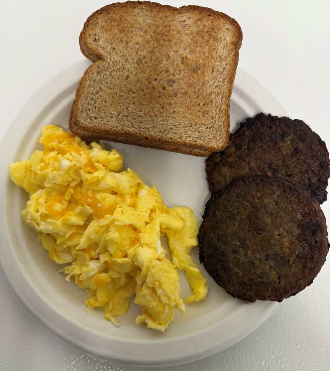 A white plate topped with scrambled eggs toast and sausage patties