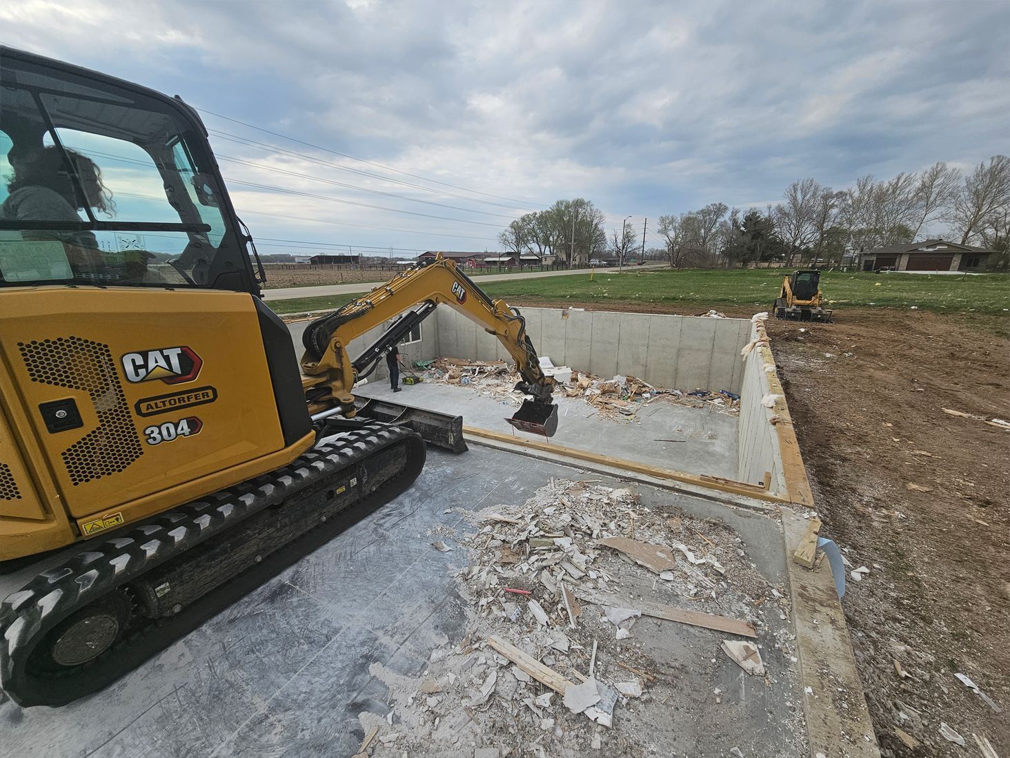A cat excavator is demolishing a concrete foundation.