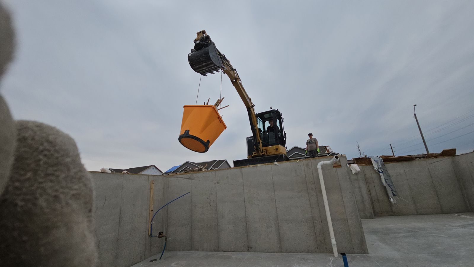 A construction site with a yellow bucket being lifted by a crane.