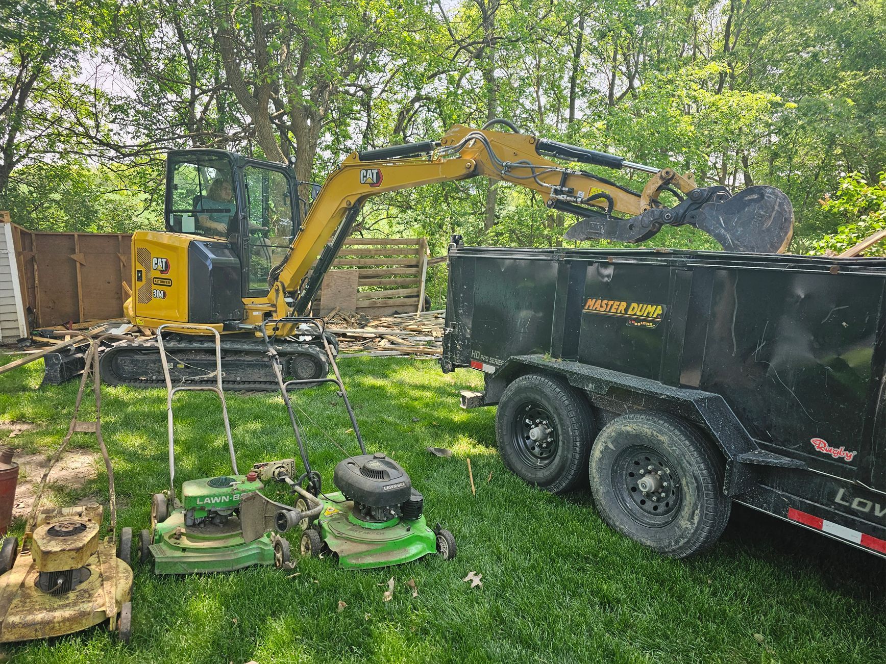 A yellow excavator is loading a dumpster into a trailer.