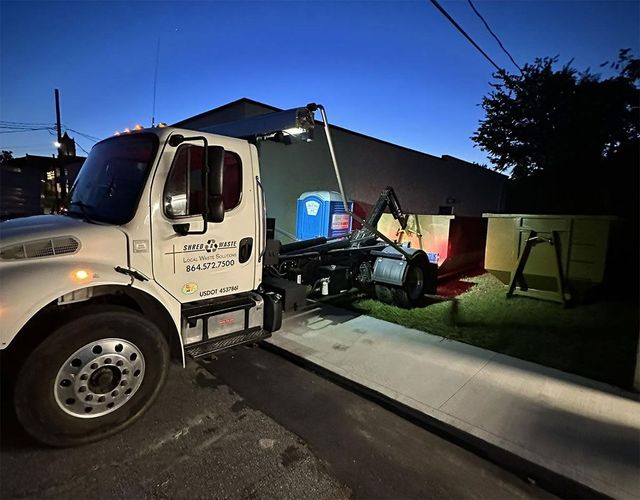 Utility truck parked by a house at dusk, with workers and equipment near the driveway and lawn.