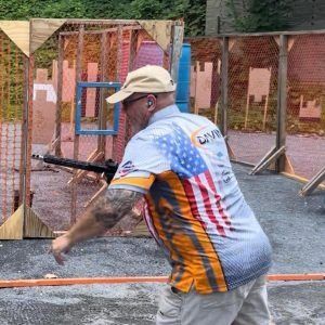 Man aiming a handgun at an outdoor shooting range with wooden target frames and safety barriers