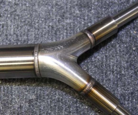 Close-up of a polished metal Y-shaped pipe junction on a gray fabric surface