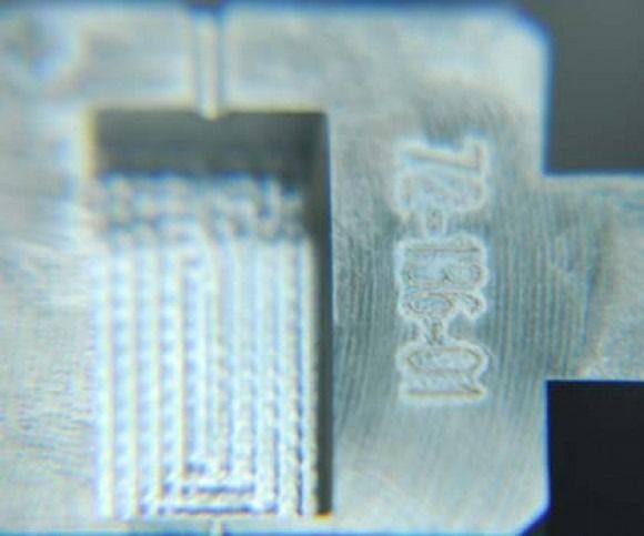 Close-up of a metal connector or chip component with etched markings and a blue-gray finish.