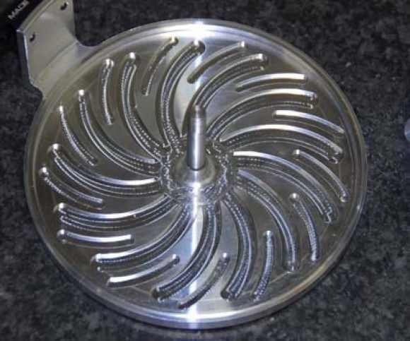 Shiny metal impeller with curved blades on a dark countertop