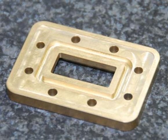 Gold metal rectangular plate with a central cutout and multiple screw holes on a speckled gray surface