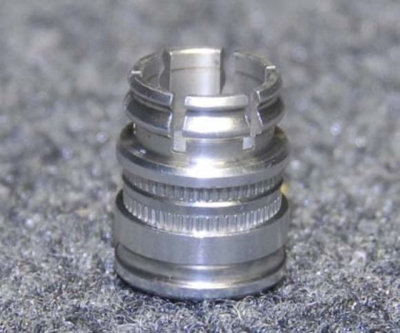 Small silver metal cylindrical part with ridged bands, resting on a gray fabric surface