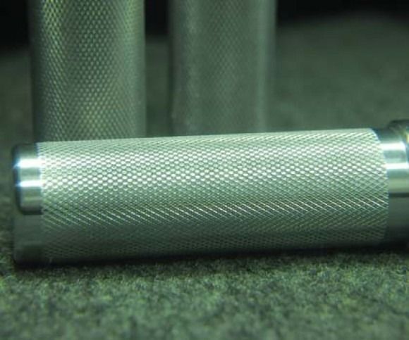 Silver knurled metal handle lying horizontally on a green surface, with blurred rods in the background