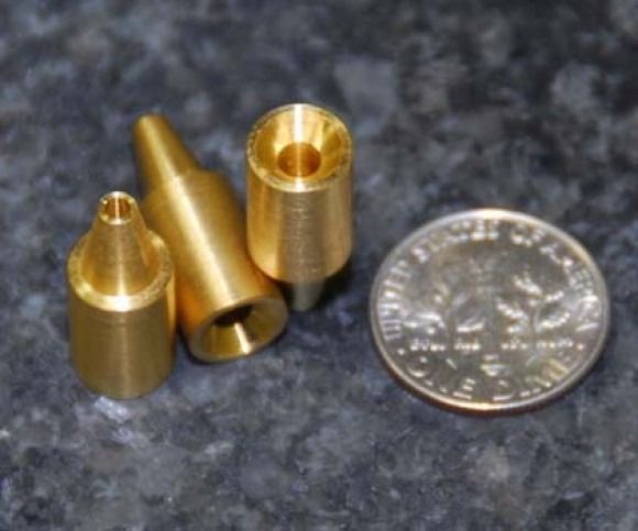 Small brass machine parts beside a U.S. quarter on a dark surface