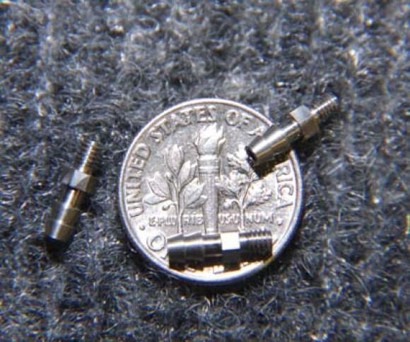 Three tiny metal drill bits arranged around a U.S. quarter on a gray textured surface